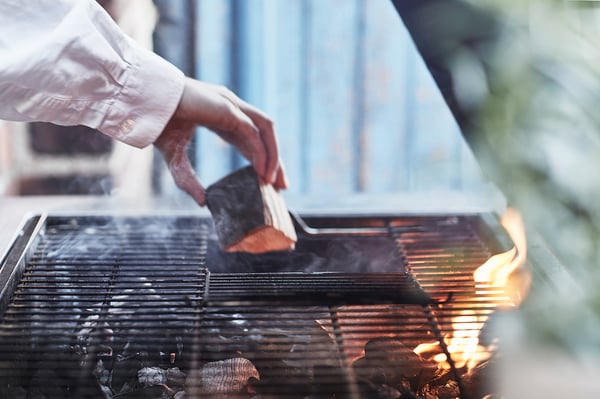 Hand grills food on modern silver bbq. Flames visible beneath metal grate.