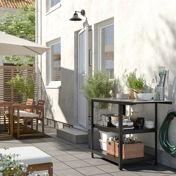 Modern outdoor kitchen with GRILLSKÄR table, plates, and plants beside house.