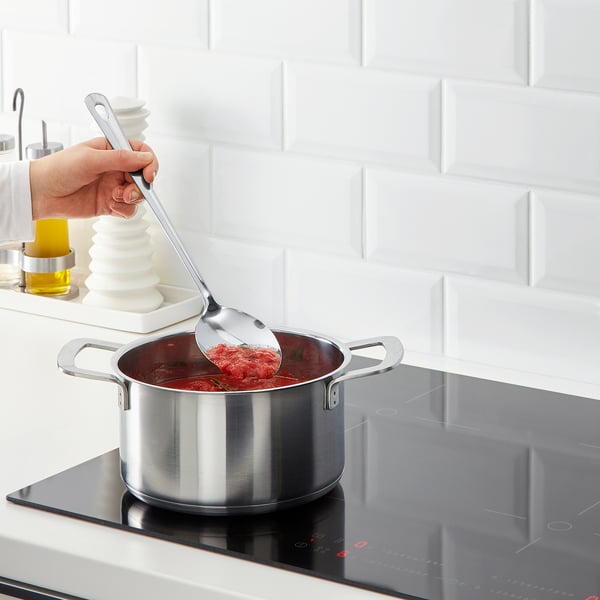 Cook stirring red sauce on modern stove.