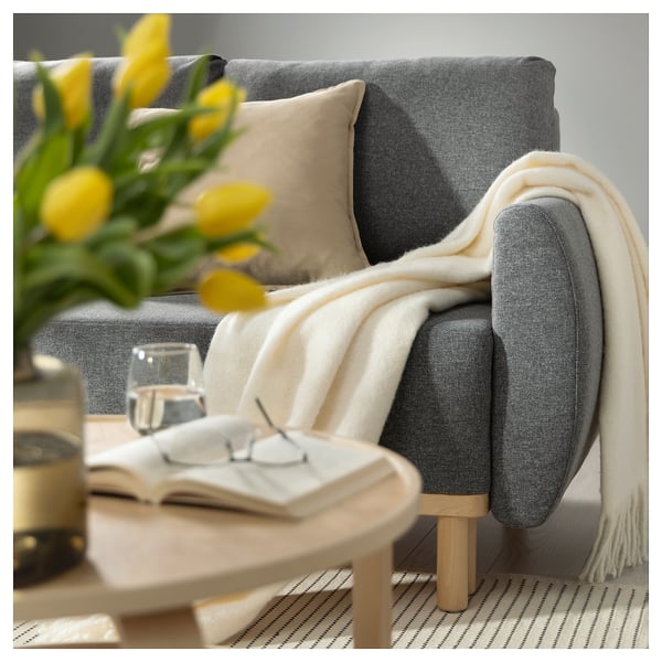 Cosy living room: grey sofa with throw, neutral pillows, yellow tulips, books, glass on table.