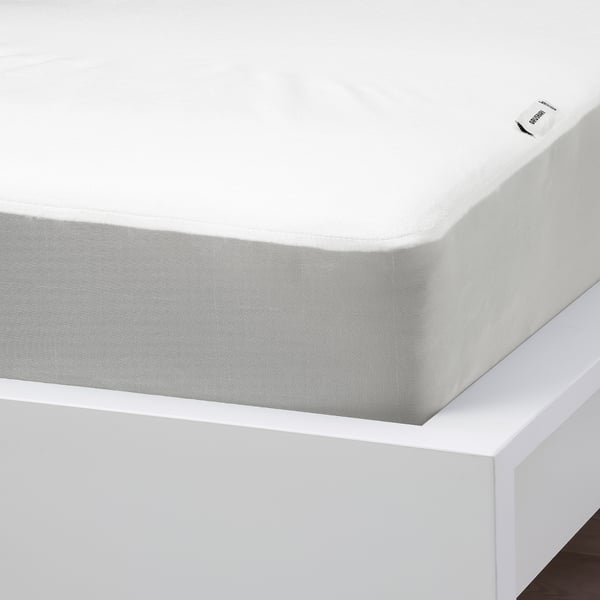 Waterproof mattress protector with patterned edge on white bed.