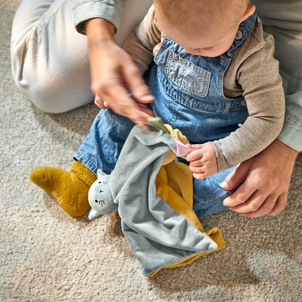 A baby sits on a carpet, holding a comfort blanket with a soft toy, suitable for play and cuddling.