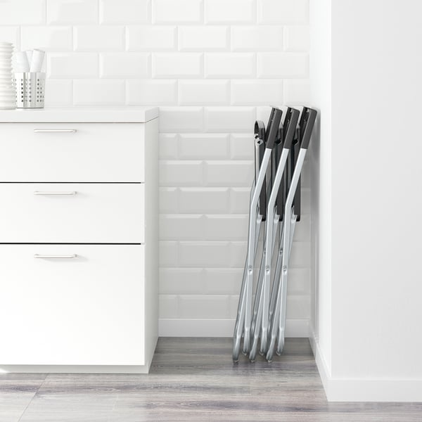 Foldable chairs stacked against white tiled wall; suitable for space-saving.