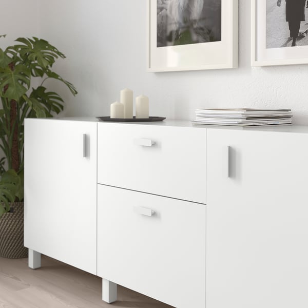 White cabinet with smooth handles, candles, and plant. Modern, functional kitchen storage.