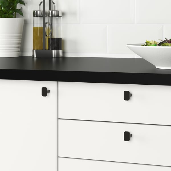 Modern kitchen cabinets with black HACKÅS knobs, smooth to touch, on white drawers with black countertop.