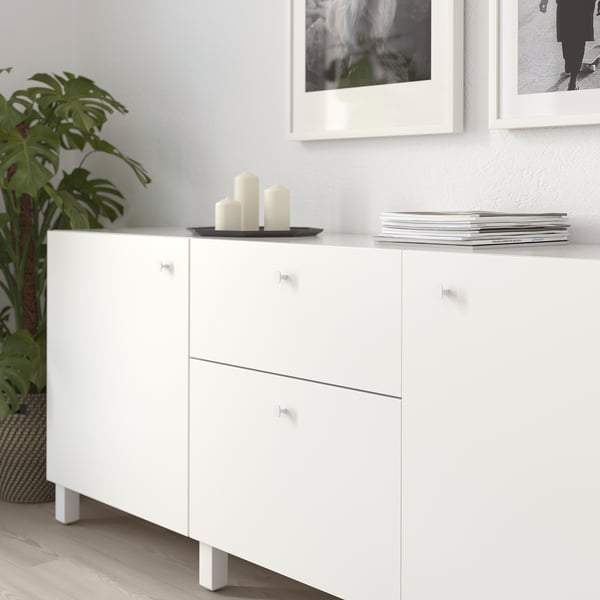 White cabinet with two drawers and handles, holding candles and books.