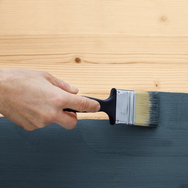Person applies dark paint on wooden surface using a brush.