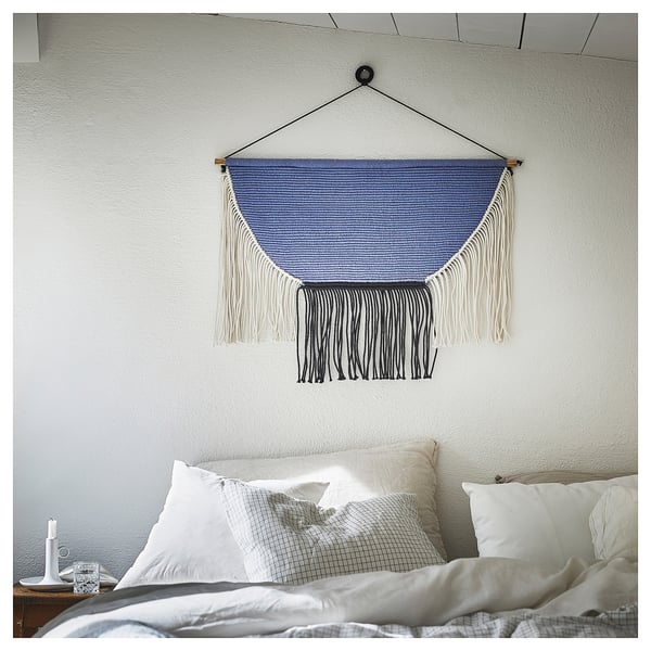 Modern bedroom with light bed and blue-black HÄNGALM wall hanging.