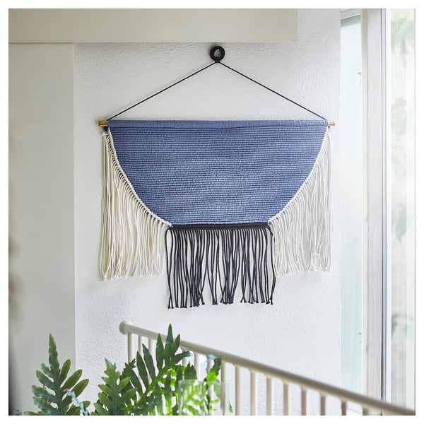 Hovering macramé by sofa, blue hanging textile with fringes, wall art.