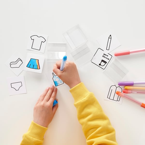 Childs hands in yellow sleeves colour with blue marker on label cards for organising.