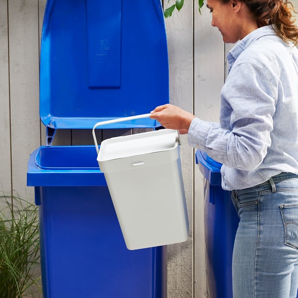 Person discarding white waste into a blue recycling bin. The person wear a light-colored shirt and jeans.