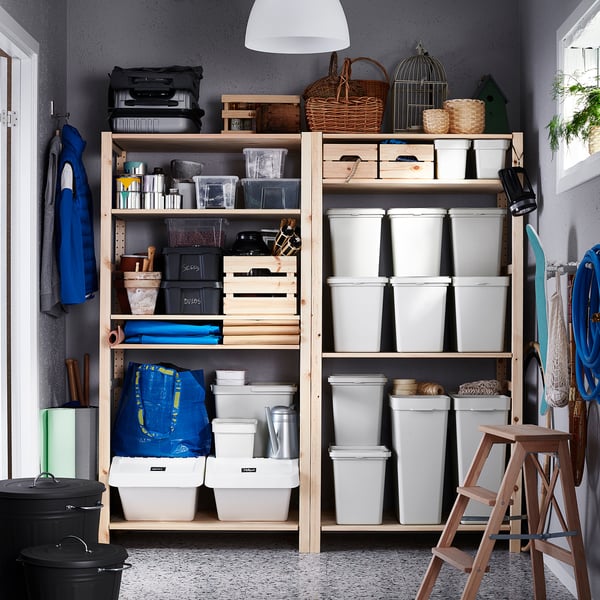 Organised storage room with shelves filled with light grey HÅLLBAR bins and various items. Blue accents and wooden crates.