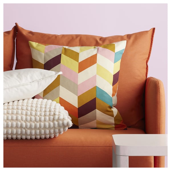 Vibrant throw pillows on orange couch, one with multicolor zigzag pattern, another with white bobbles, adding texture and style.