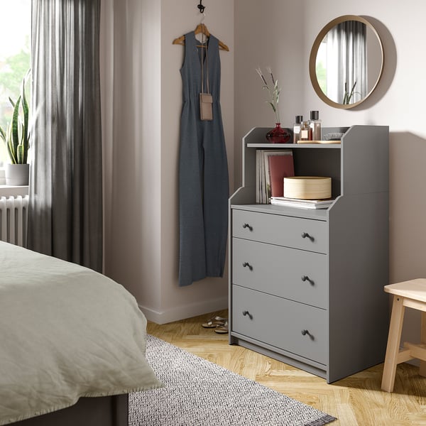 Bedroom with modern decor, featuring a grey HAUGA dresser, hanging blue dress, round mirror, and potted plant.