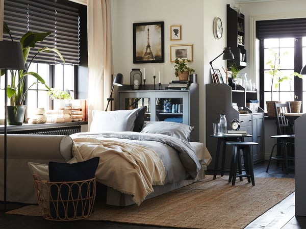 Modern bedroom with white bed, wooden floor, and black HAUGA cabinet; neutral tones, natural light.