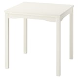 Depicts a white HAUGA dining table, a square wooden design with a smooth top and four sturdy legs, perfect for small spaces.