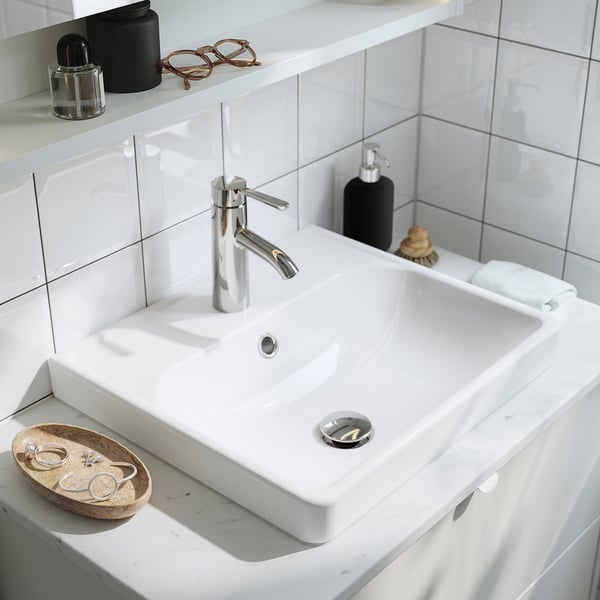 Modern white bathroom sink with chrome tap, soap dispenser, and accessories. Two drawers beneath for storage.