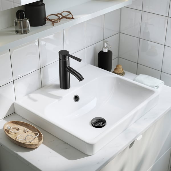 Modern white bathroom sink with black tap. Sleek, minimalist design, small fixtures.