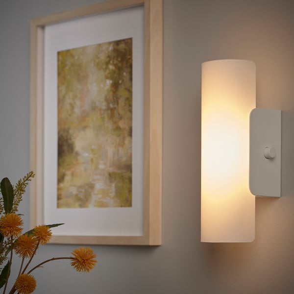 Wall-mounted lamp with frosted glass shade emits soft, dimmable light, suitable for bathrooms.