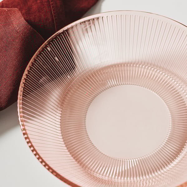 Close-up of a pink, ribbed glass plate on a white surface. The plate has a textured design and appears sturdy, reflecting light subtly.