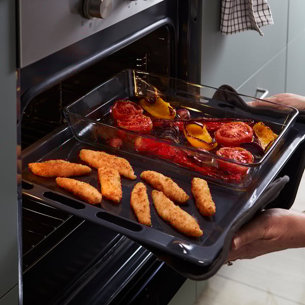 Person holding oven tray with breaded fish and roasted vegetables.