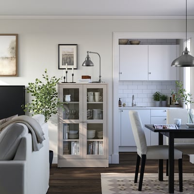 Modern living space with HAVSTA light wooden display cabinet, white kitchen, dining table, and grey sofa.