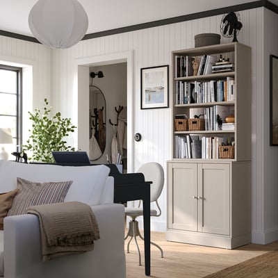 Cosy living room with white couch, bookshelf, potted plant, and laptop.