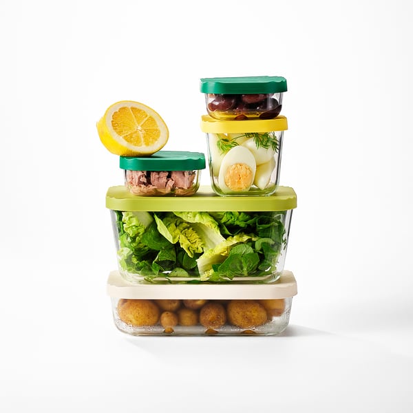Multiple glass containers with colorful lids stacked, filled with leftover food, efficiently saving space in storage.