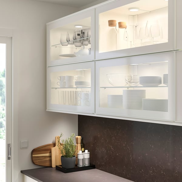 Modern kitchen with glass cabinets, dark counter, plant, and accessories.