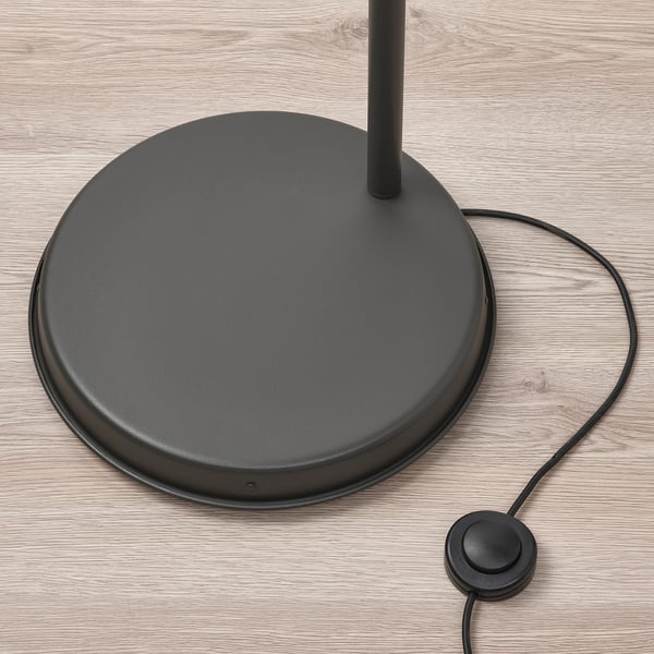Circular black floor lamp base on wooden floor with power cord and foot switch, high quality finish.
