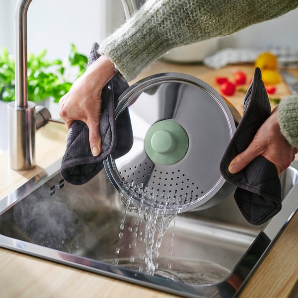 Person rinses pots under tap, showcasing the non-stick pan and lids easy-clean feature.