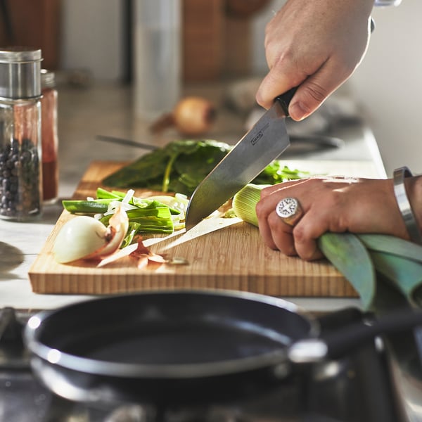 Person chops vegetables on a cutting board using a knife. A small non-stick frying pan sits nearby on a stove, ready for cooking.