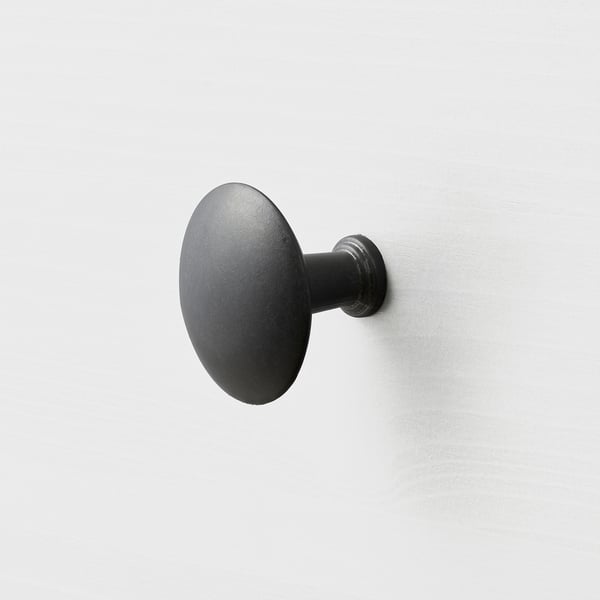Black circular wall-mounted hook, smooth and sleek, modern design. Attached firmly to a plain wall.