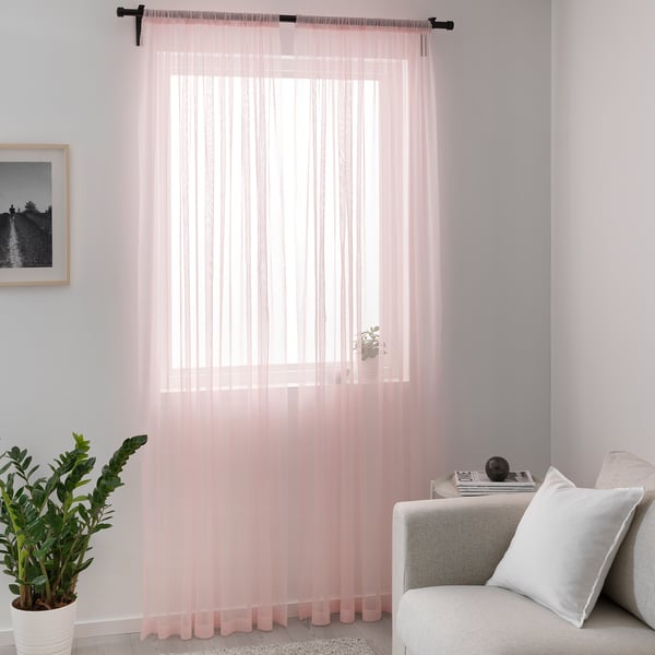 Pink curtains frame window, lighting cosy living room with couch & plant.