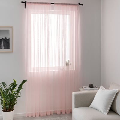 Pink curtains frame window, lighting cosy living room with couch & plant.