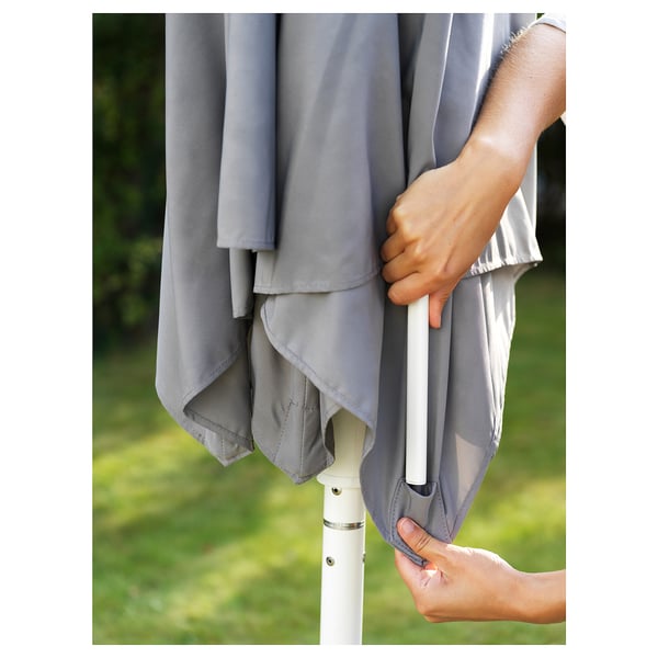 A person adjusting a grey, collapsible HÖGÖN parasol with a white handle outdoors.