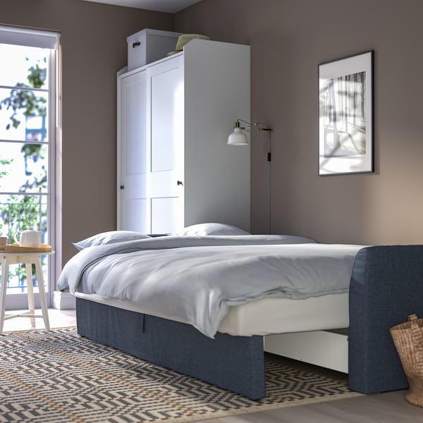 Modern bedroom with gray walls, white bed, blue headboard, and rug. Wardrobe and picture above bed.