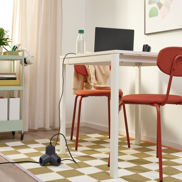Home office with laptop, bottle, headphones, and HORNFELS extension cord on white desk. Red chair in front.