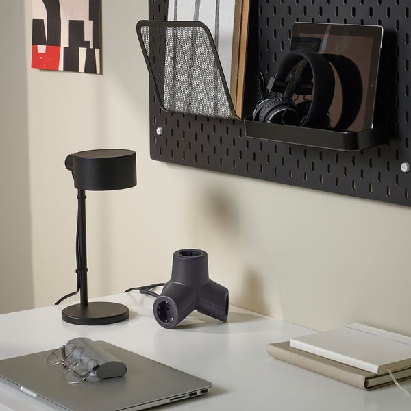 A desk setup showing a black 4-way extension plug, a lamp, and computer accessories.