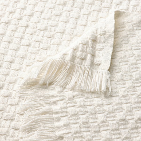 Close-up of a cosy, off-white recycled polyester blanket with a textured basket weave pattern and playful fringes.
