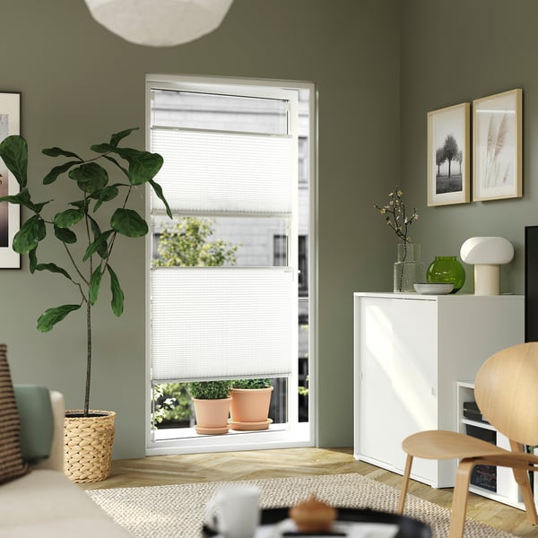 Modern living room with window blind, plant, cabinet, photos, and desk setup.
