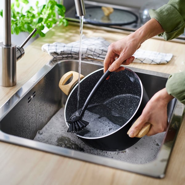 Person washing a non-stick, induction-compatible frying pan with a grip handle.