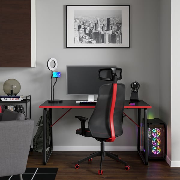 Modern gaming setup: HUVUDSPELARE desk, red/chair, dual monitors, ring light, bookshelf & sofa.