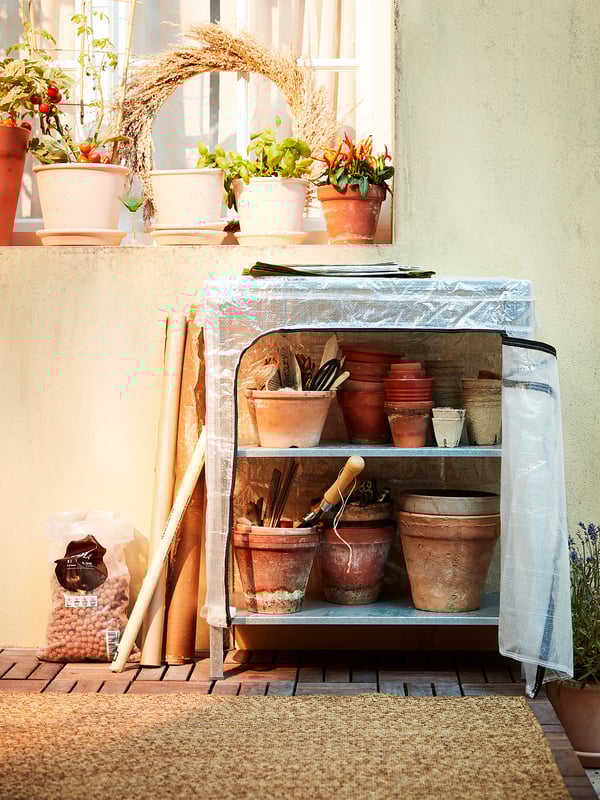 Small greenhouse storage: HYLLIS silver steel unit, clear cover, terracotta pots, plants on sunny balcony.