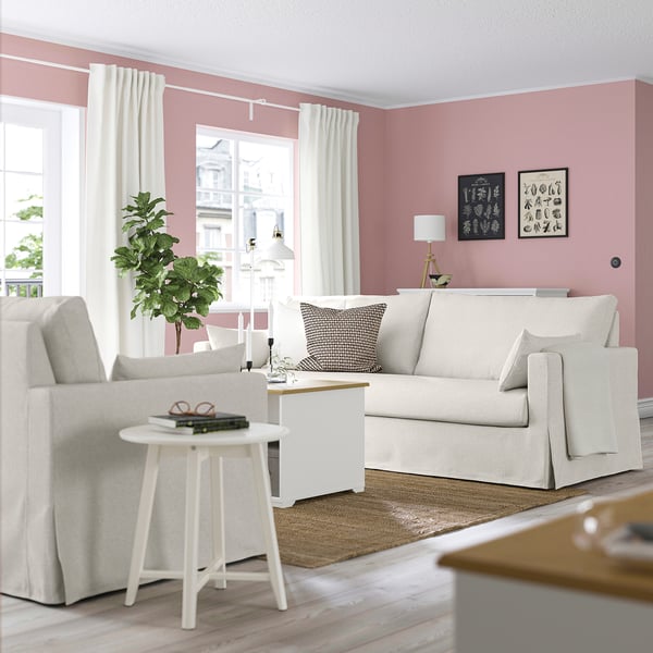Cosy living room with beige HYLTARP sofa, patterned throw pillow, pink walls, and modern decor.