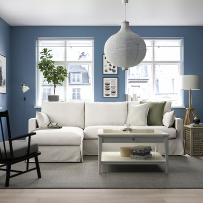 Stylish HYLTARP sectional sofa in blue-walled living room with storage chaise, large rug, pillows, lamp, and plant.