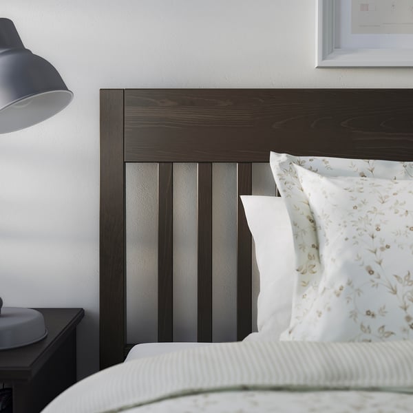A dark wooden bed frame with a headboard, white pillows, and a grey lamp on a dark bedside table.