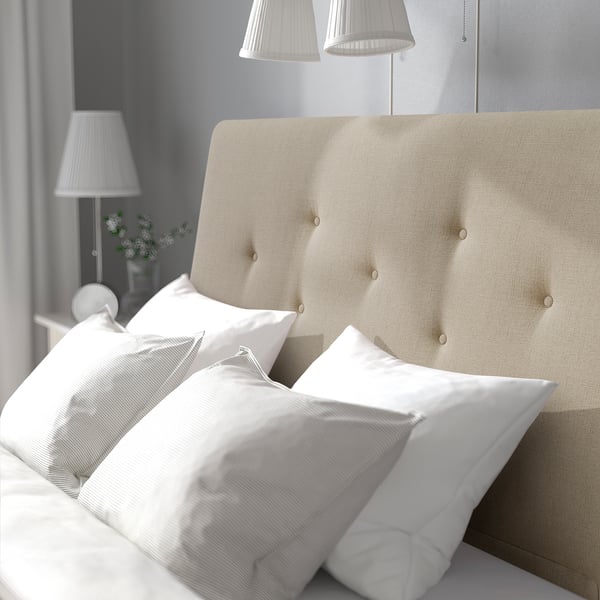 Neutral-tone bed with sloping headboard, soft pillows, and bedside lamps. Shows comfort and relaxation.