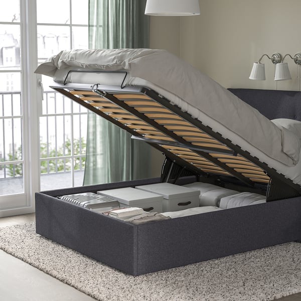 Bed with raised upholstered headboard displays storage underneath containing boxes and folded items.