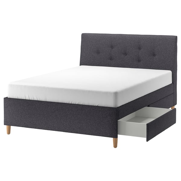 Modern grey upholstered bed with slanted headboard, wooden legs, and storage drawers for compact spaces, IDANÄS series.